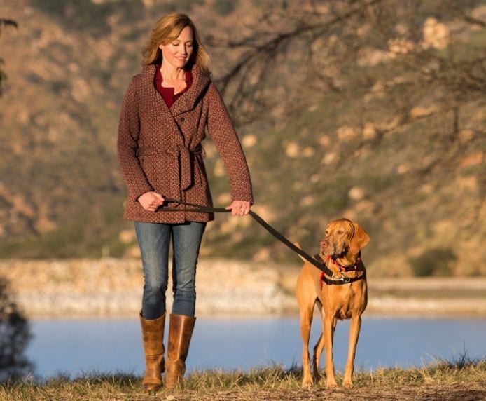 A dog wearing a Halti Front Control Harness being walked by a woman near a lake