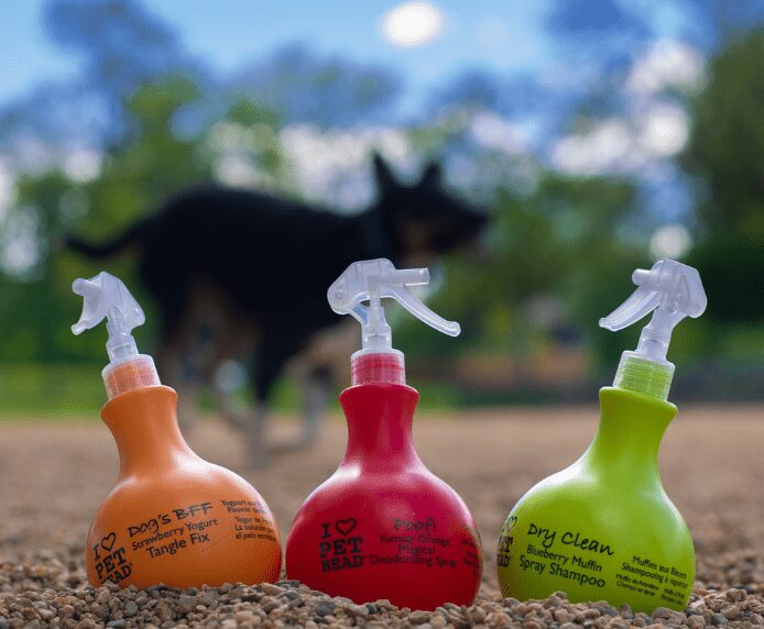Three bottles of Pet Head spray in the garden with a dog in the background