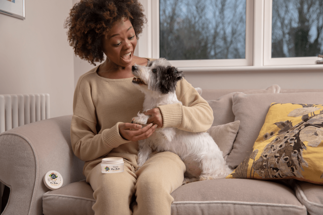Image of woman holding small dog on couch enjoying paw butter