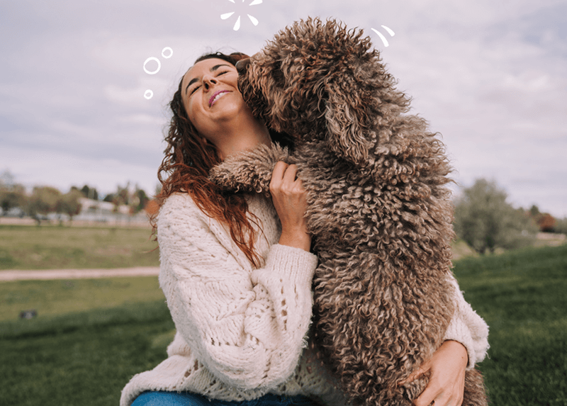 A very fluffy dog kissing a woman in a field